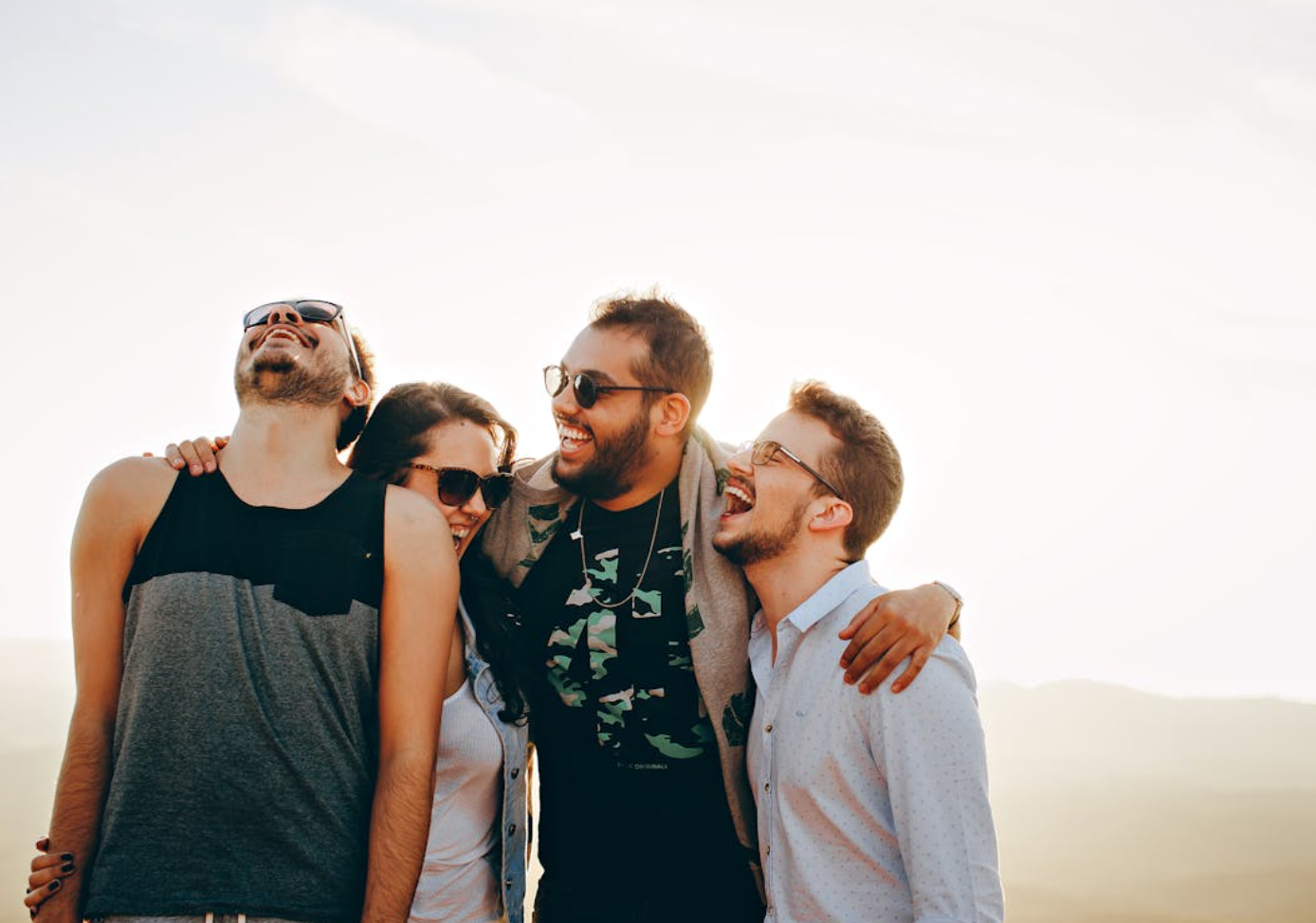 Four friends laughing and hugging; image by Helena Lopes, via Pexels.com.
